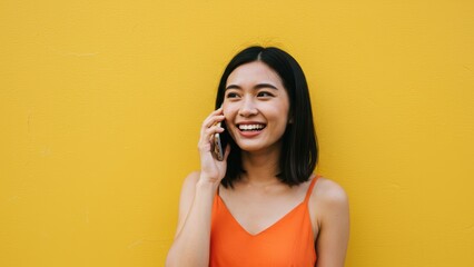 Fototapeta premium Filipino woman smiling while talking on phone against yellow wall Expresses positivity, youthfulness, and modern urban lifestyle