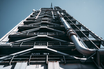 Low-angle view of a towering industrial metal structure with steel beams, pipelines, and rusted...