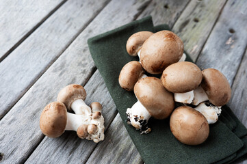 Raw brown champignon mushrooms placed on a weathered wooden surface.