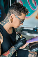Tattoo artist wearing black gloves using a tattoo machine drawing a tattoo on a client's arm in a professional studio