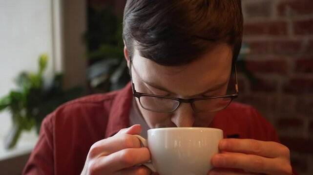 Young man enjoying matcha latte in cafe, green foam creating playful mustache on upper lip while wearing red shirt and glasses