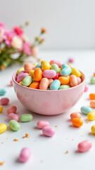 Colorful candy pebbles are scattered around a pink bowl with more of them inside on a white surface, creating an appetizing display of sweet treats.