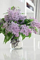 Bouquet of lilac flowers standing in glass vase on white table