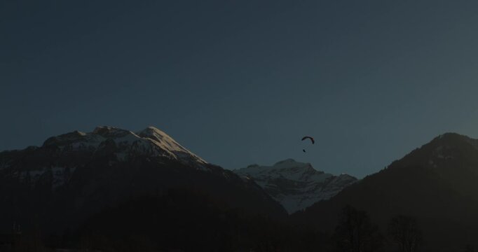 a paraglider soaring above majestic snow-capped mountains at sunset under a serene clear blue sky