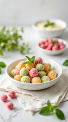 Brightly colored round candy balls in a bowl on a table with additional colorful treats in smaller bowls and fresh mint leaves in the background.