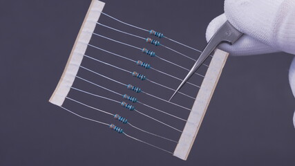 Close-up of a THT 1/4W resistor with a color-coded band pattern, positioned on a dark background. A...