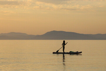 Naklejka premium Silhouette of an woman on a surfboard at sunset