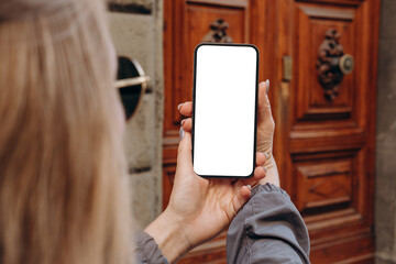 Mockup woman's hand holding using smart phone with white blank screen POV at on the background of a house on the street in Europe real estate  rent, mobile app design and advertising, online marketing