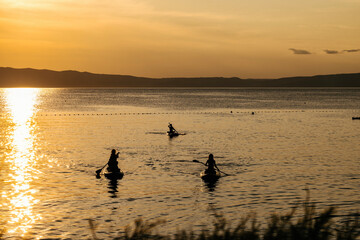 Fototapeta premium Magical sunset over Cres island, Croatia, with istrian peninsula visible across the sea while children enjoy riding their sup boards