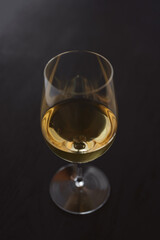 White wine in a wineglass on black oak table with copy space