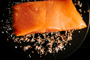 Fresh organic trout fillet displayed on black board surrounded by assorted seeds for a healthy meal...