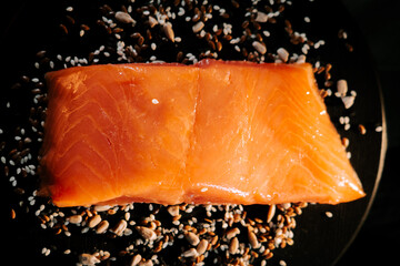 Fresh organic trout fillet displayed on a black board with scattered seeds and grains
