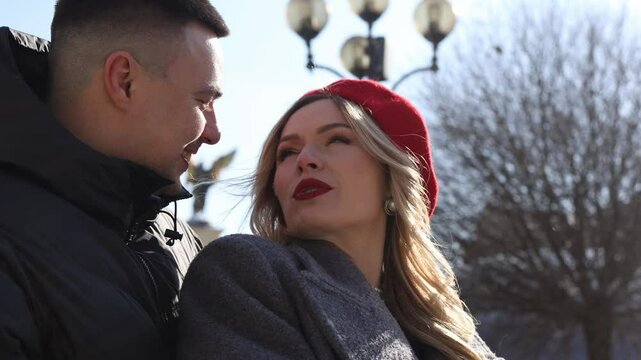 A young couple hugs and cuddles in the winter sun against the backdrop of a city street. The girl wears a red beret in Paris