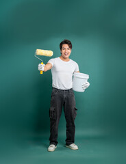 A painter in a white shirt, black pants, and white gloves holds a paint roller and bucket against a solid green background, ready to paint a room.
