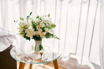 Wedding bouquet stands on a glass table in a room against the background of a white curtain