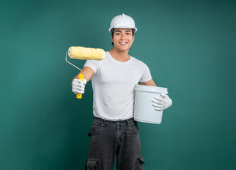 Ready to Renovate: Confident painter with roller and paint bucket on a vibrant teal backdrop,...