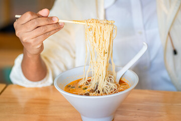 Crop anonymous female with chopsticks eating yummy ramen soup with noodles and meat in black bowl...