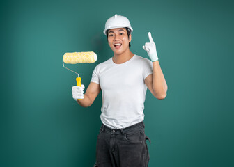 Enthusiastic painter with roller. Pointing upwards, wearing hard hat and protective gloves against...