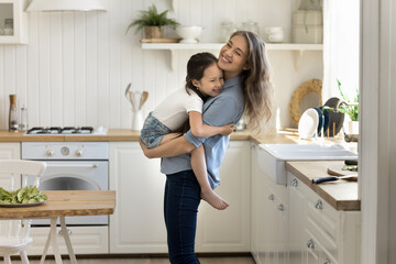 Bonding and comfort. Young single mom happy homeowner buyer renter stand in new modern well equipped cozy kitchen hold little girl daughter share joyful family moments with kid enjoy cooking wellbeing