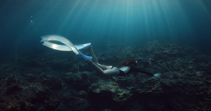 Freediving with woman in tropical sea over corals and sun rays in Raja Ampat