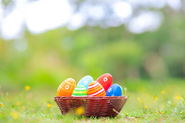 A wicker basket filled with colorful Easter eggs sits on fresh green grass, surrounded by a blurred natural background.