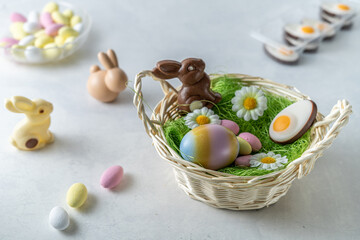 Chocolate Easter bunny in basket. pastel colored almond sweets and eggs on white marble stone table. Light and airy, high angle view, copy space