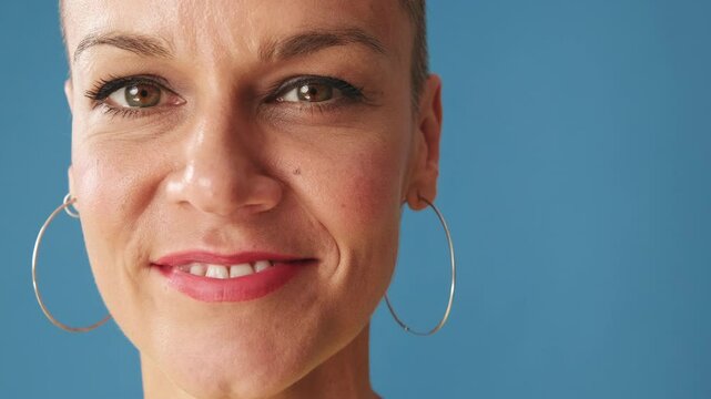 Portrait close up of smiling young bald woman wearing yellow t-shirt looking at camera, isolated on blue background in studio
