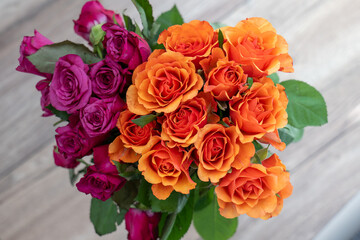 A bouquet of vibrant roses, one in deep purple and the other in bright orange. The roses are fresh and beautifully arranged on a neutral wooden background.