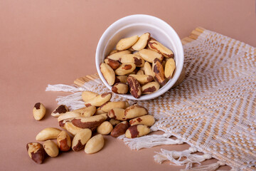 Shelled Brazil nuts in a white ceramic bowl and mocha background with space for text. Healthy eating.