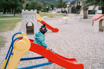 Little girl slides down a colorful slide in the playground. Side view