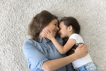 Warm and tender embraces. Peaceful view from above of happy loving young mom and little daughter preschooler lying on fluffy carpet at home hug cuddle with closed eyes enjoy cozy sweet family moment
