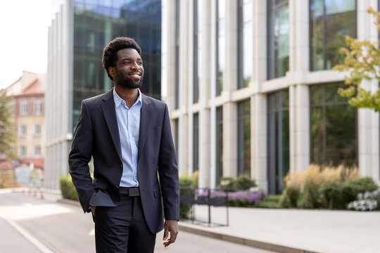 Successful businessman walking through the city in a business suit. African American man smiling happily, outside an office building.