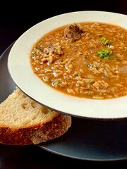 Georgian soup. Kharcho with rice, tomatoes, beef, garlic and herbs in the plate on black table Traditional Caucasian food spicy soup with lamb, tkemali and rice. Man showing pieces of meat with spoon.