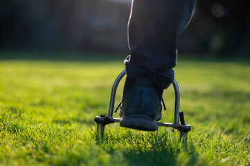 Man uses a hand aerator in the garden to punch out holes which improves the ventilation of the lawn.