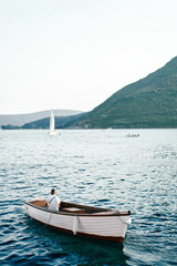 Fisherman sits in a white fishing boat and looks out to sea. Back view