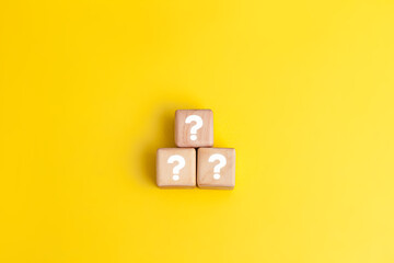 Three wooden blocks with white question marks stacked in a pyramid shape against yellow background....