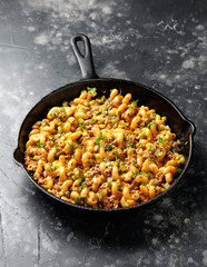 Cheeseburger Pasta with ground beef, melted cheese and gherkins in a iron cast pan