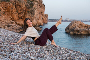 Young woman enjoying a playful moment on a rocky beach at sunset in a coastal town