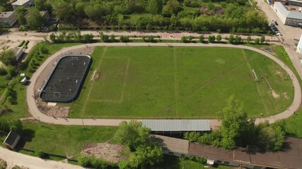 Professional athletes running on circular track surrounding green soccer field, aerial perspective showcasing athletic performance and training dynamics