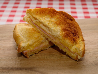 A toasted sandwich sliced in half, revealing layers of ham and cheese, resting on a wooden board. The vibrant red and white checkered background adds a cozy touch
