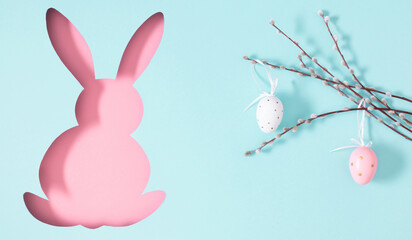 Easter concept. On pastel blue background image of cute Easter bunny with pussy willow branches with painted eggs, top view, flat lay.