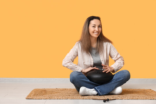 Beautiful mature woman with glucophone sitting on carpet near yellow wall