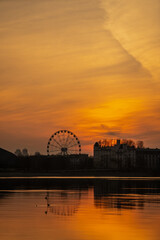 Obraz premium Latvian sunset with Riga sunset silhouette city scape. Calm small european city skyline of ferris wheel and modern building silhouettes of shadows in evening orange sun skies