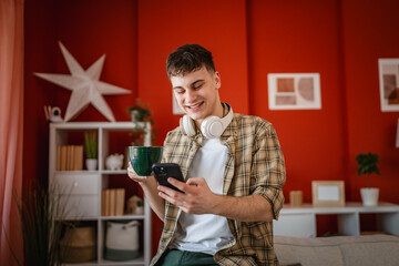 young man relaxing with mobile phone and cup of coffee at home