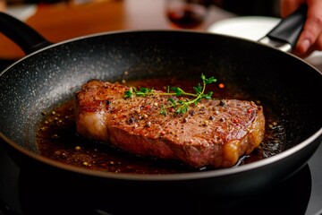 Fototapeta premium A freshly cooked steak lies sizzling in a frying pan, surrounded by fragrant herbs and spices, highlighting the golden-brown crust. The warm kitchen atmosphere enhances the inviting scene