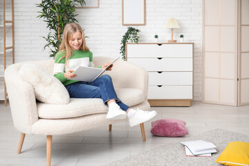 Cute little girl reading book while sitting on sofa at home