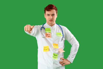 Male doctor with reminders pointing at viewer on green background