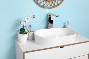 Modern sink with bath supplies on countertop near blue wall in bathroom