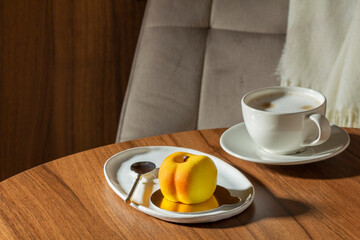 Mousse cake with peach filling covered with velvet glaze and a cup of latte on a table in a cafe.