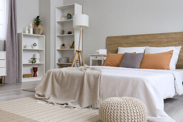 Interior of stylish modern bedroom with big bed, shelving units, lamp and bedside tables